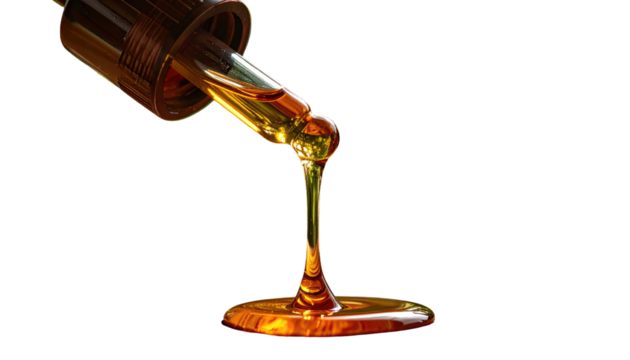 Golden liquid drips from a glass dropper, forming a small puddle against a dark, stark background