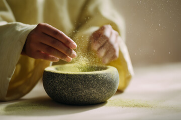 Person sprinkling matcha powder from bowl on wooden table  