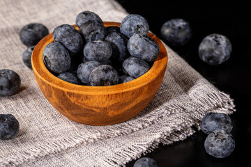 A wooden bowl overflowing with juicy blueberries on a soft linen napkin