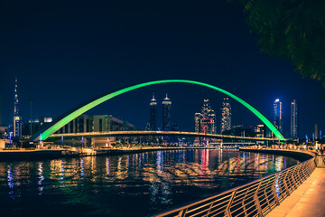 Dubai downtown night city skyline. Bridge over the canal. Modern skyscrapers and lights are reflected in the water.