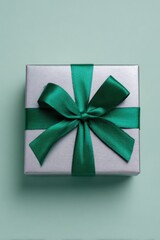 A silver square gift box sits centered on a pastel background, wrapped with an emerald green satin ribbon tied into a large decorative bow on the top