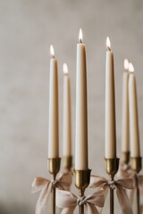 Several tall ivory taper candles are lit and placed in gold-toned brass holders, each wrapped with soft neutral colored fabric bows, creating a warm festive ambiance