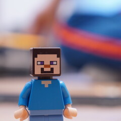 Naklejka premium Close-up of a LEGO Minecraft character figurine, known as Steve, with a blue shirt and square features, set against a blurred background