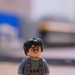 Fototapeta premium Close-up of a Lego Harry Potter minifigure with his signature round glasses and black hair, standing in a room with a blurred background