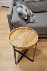 Wooden Round Coffee Table with Metal Legs Next to a Sofa, Pillows, and Wooden Floor
