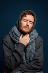 Fototapeta premium Man in Hoodie and Scarf Holding Throat in Painful Expression