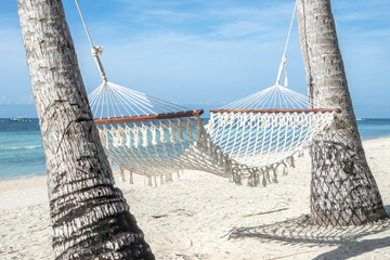 Stunning views of an empty beach, palm trees, and a hammock on a wonderful island. Clear, sunny day, warm sunlight. No people, outdoors. Concept of leisure and travel