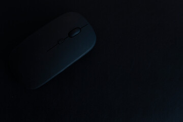 A black computer mouse sits on a dark surface