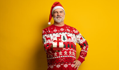 Obraz premium Merry mature man wear red warm knitted sweater Santa hat posing hold present box with gift ribbon bow isolated on yellow