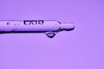 A pipette with serum demonstrating its juicy texture on a purple background.