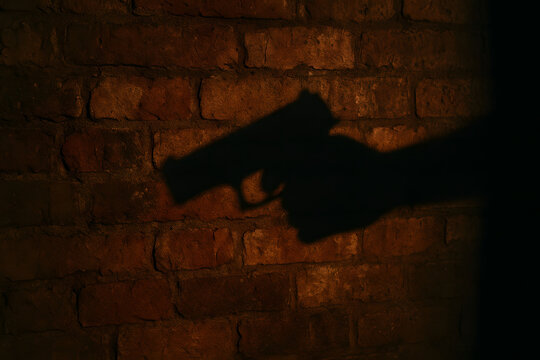 Shadow of hand holding gun on brick wall background, dark crime mystery concept, cinematic lighting for thriller movie poster, suspense tension atmosphere, fear danger security concept composition