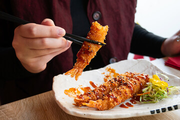 A woman eating deep-fried shrimp tempura in a restaurant.