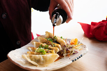 A woman pours soy sauce over gyoza, Japanese dumplings at a restaurant.