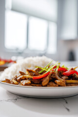 Plate of stir-fried chicken with bell peppers and scallions served alongside white rice.