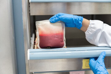 Close up scientist hand wear blue gloves holding red blood bag in storage refrigerator at blood bank unit laboratory.Blood bags received from blood donations used in patients.Save life medical concept