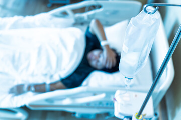 Close up set iv fluid intravenous drop saline drip in hospital room with blurry patient woman on hospital bed.Medical treatment emergency patient.Caregiver and hopeful concept.