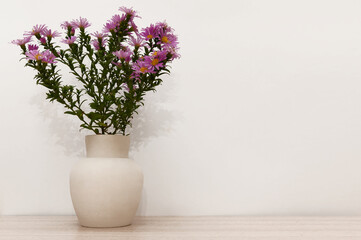 There are lilac flowers in a white clay vase on a wooden background.