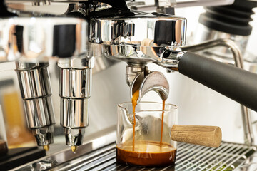Coffee machine brewing espresso in to glass cup.Barista while preparing and working with coffee machine and making espresso coffee from arabica coffee beans.Americano pouring into a measuring cup.