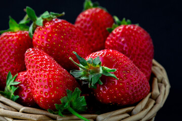 Fresh ripe strawberries collected in a woven basket against a dark background, showcasing their vibrant red color and fresh green leaves