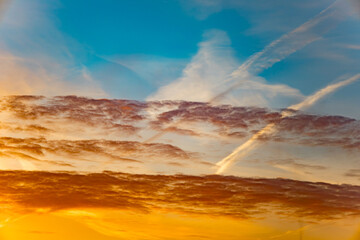 Obraz premium Colorful sunset sky with clouds and streaks of vapor in the evening light over a serene landscape