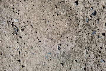 Surface of a weathered concrete wall showing unique texture and small holes in natural light at midday