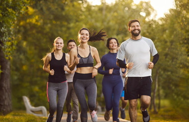 Strong fit team of runners running marathon, morning workout of confident athletes in summer park. Sporty people in sportswear training outdoor together with high motivation. Vitality concept