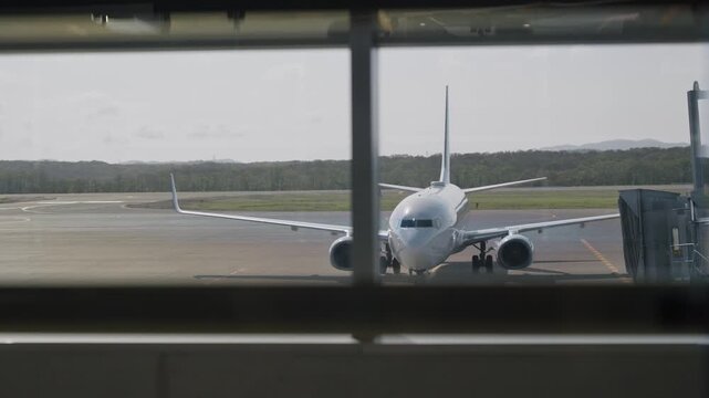 View from terminal gate window on airplane arriving at airport tarmac or runway. Plane approaching arrival gate for boarding or disembarking passengers in flight reaching jetway bridge tunnel