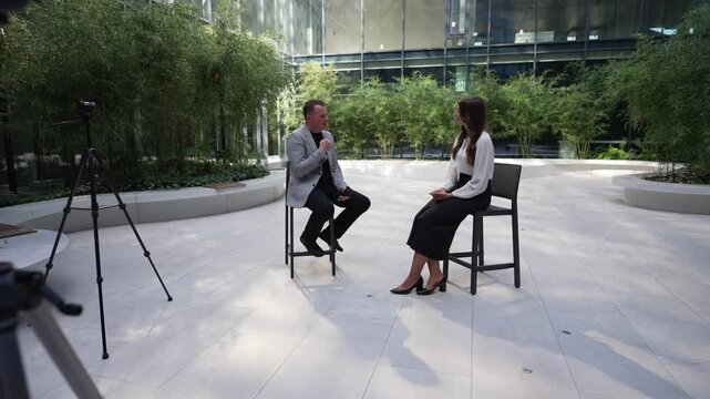 Two professionals talking, surrounded by cameras and greenery. Business conference concept.