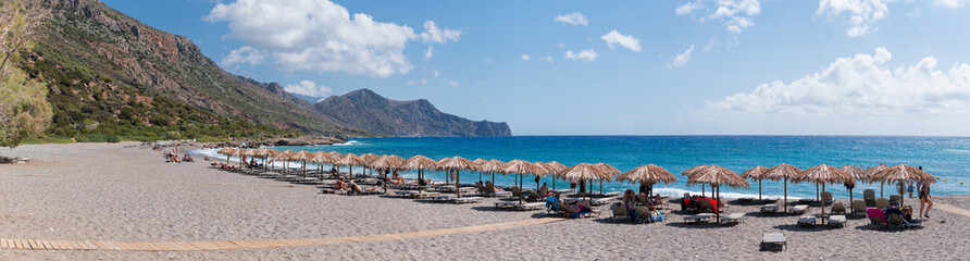 Panoramic View of Beach with Straw Umbrellas and Mountains in Crete Greece