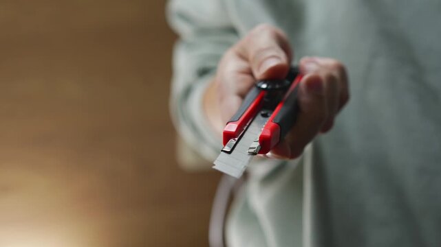 A red plastic cutter knife with a retractable blade in a person's hands