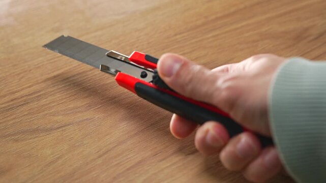 A red plastic cutter knife with a retractable blade in a person's hands