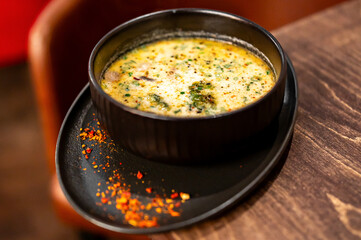 A rich, creamy bowl of soup with herbs and spices, served in a black bowl on a rustic wooden table. Close-up food photography.