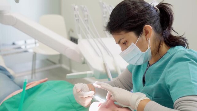 Professional female dentist in a modern clinic performing a dental treatment on a patient lying in the chair for oral hygiene