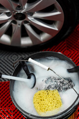 Yellow sponge and brushes in soapy water ready for car detailing. Foam-filled bucket with cleaning tools ready for car detailing. Car cleaning gear prepared in foamy water.