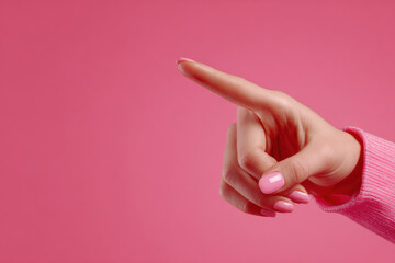 A woman's hand points at something on a pink background, close-up.