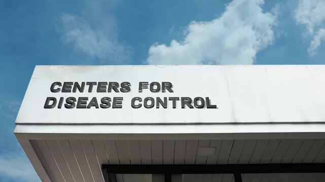 Centers for Disease Control word sign prominently displayed on the professional, secure facade of a major government medical or research facility beneath a clear blue sky, signifying the national