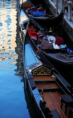 Traditional black gondolas moored in narrow canal with reflections of colorful Venetian buildings on calm water surface in Venice, Italy, detail of elegant boats with copy space