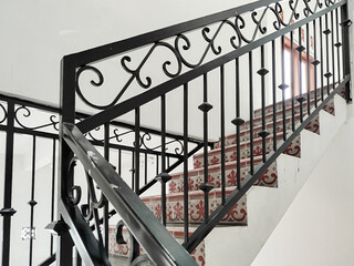 Interior staircase with black wrought iron railing and patterned tiles.