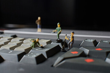 Miniature plastic workers pretending to fix an old computer keyboard against a black background