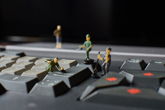 Miniature plastic workers pretending to fix an old computer keyboard against a black background