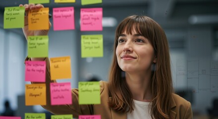 Creative professional woman brainstorming ideas with colorful sticky notes on glass board. Businesswoman working on project management and strategic planning in modern office