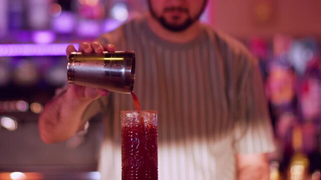 Preparing liquor. Serving cocktail. Male barman adding red liquid from shaker to glass. Garnishing aperitif with green hot pepper pod.