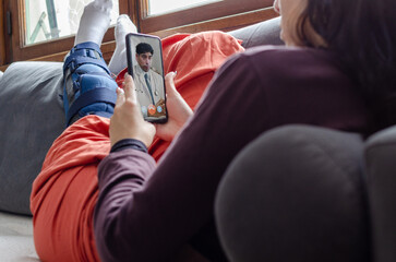 Young woman with broken leg laying on a couch having a video call with a doctor.