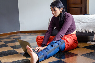 Young woman with a broken leg working from home with a laptop.