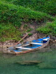 Obraz premium Old wooden boat resting on a tranquil riverbank surrounded by green vegetation in the early morning light