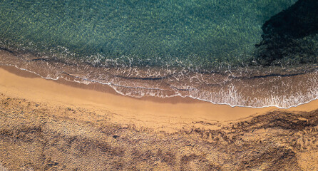 Drone aerial top view of Mediterranean coastline where turquoise sea meets golden sand, perfect natural symmetry of waves and beach.