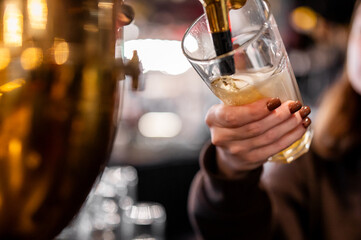 Close-up of a bartender's hands pouring a fresh draft beer from a brass tap into a clear glass in a pub or bar setting.