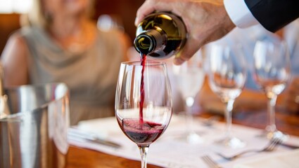 Waiter, sommelier pouring a glass of rich red wine for a customer at a lively restaurant event, enhancing the luxurious dining experience.
