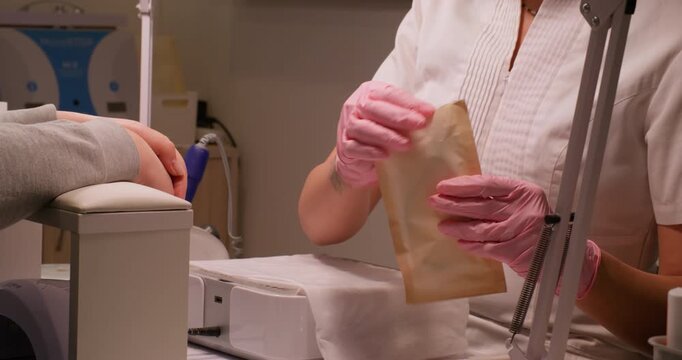 Professional manicure. Nail hygiene. Beautician female hands in sterilized pink gloves taking tools forceps getting ready for beauty service care procedure.