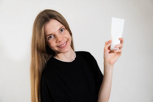 Portrait of a blonde beautiful girl on a white background. In her hands she holds care cosmetics and cream. Model is wearing a black basic T-shirt.